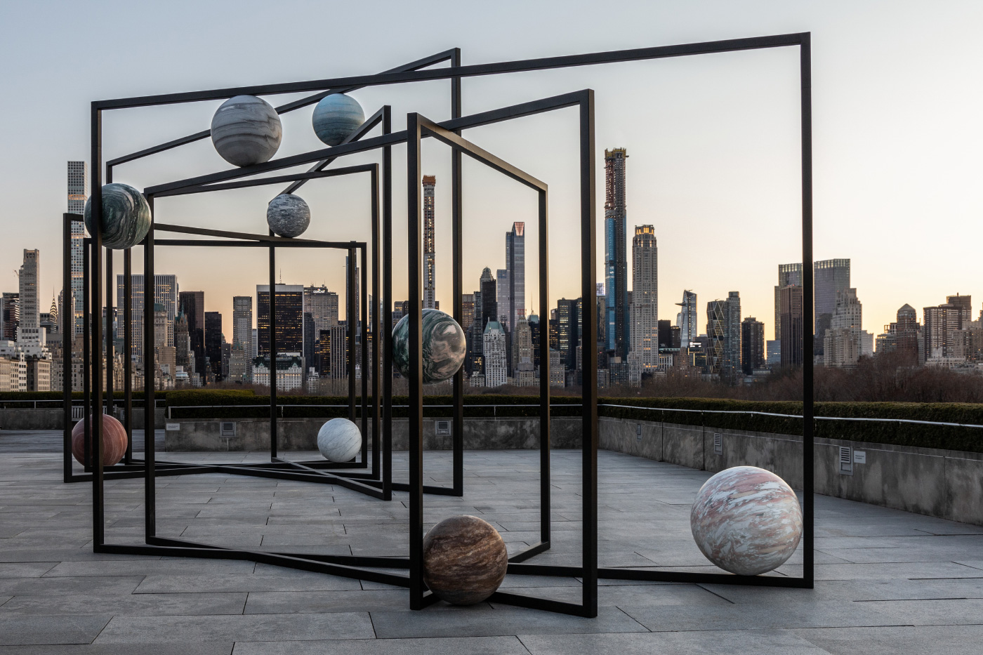 不同颜色的大石球悬挂在黑色钢架上，映衬着曼哈顿的天际线