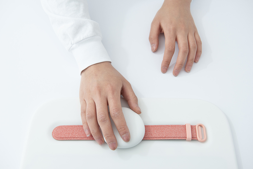 照片中的手拿着一个白色的球状物体在粉红色的腕带上。