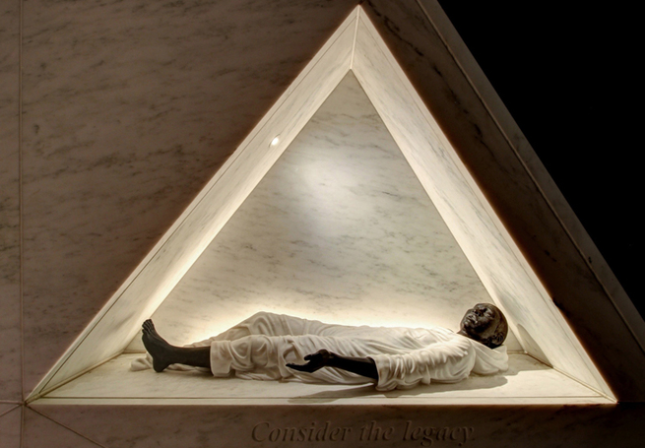 一尊斜靠在三角形镂空结构中的黑人雕塑的照片。