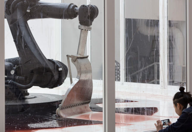 一个机器人手臂，刮刀末端在地板上的红色液体中扫地