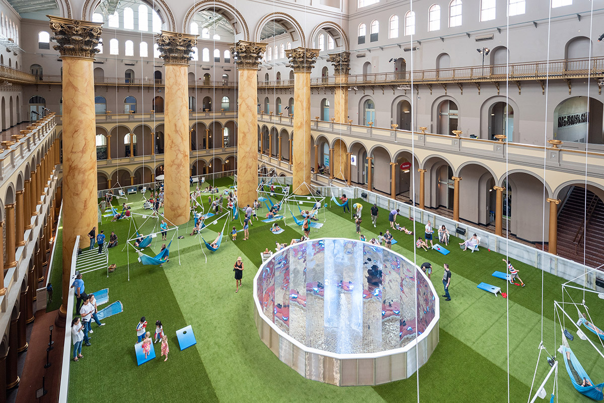 鸟瞰国家建筑博物馆巨大的大厅，柱子和绿色的地毯，人们在蓝色的吊床和躺椅上闲逛