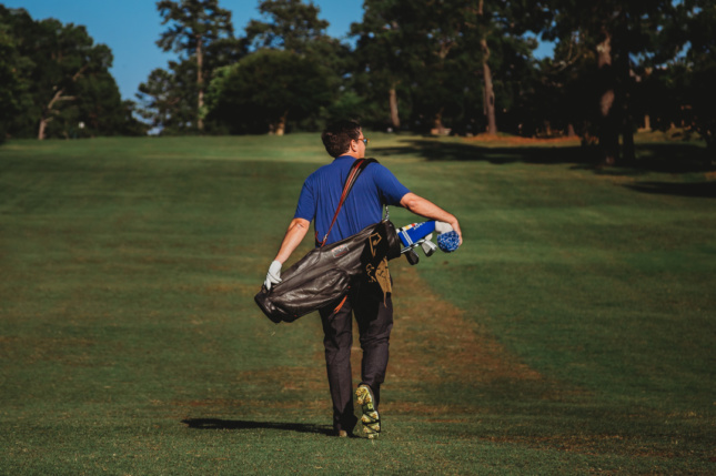 一个男人提着包走在高尔夫球场上