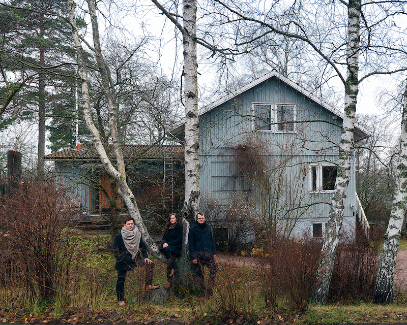 三位建筑策展人站在树林里的木屋前