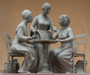 两个女人坐在桌子旁，第三个站在桌子后面的雕像照片