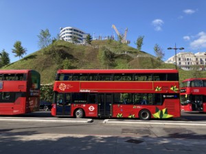 london tour buses in front of a manmade hill, the marble arch mound