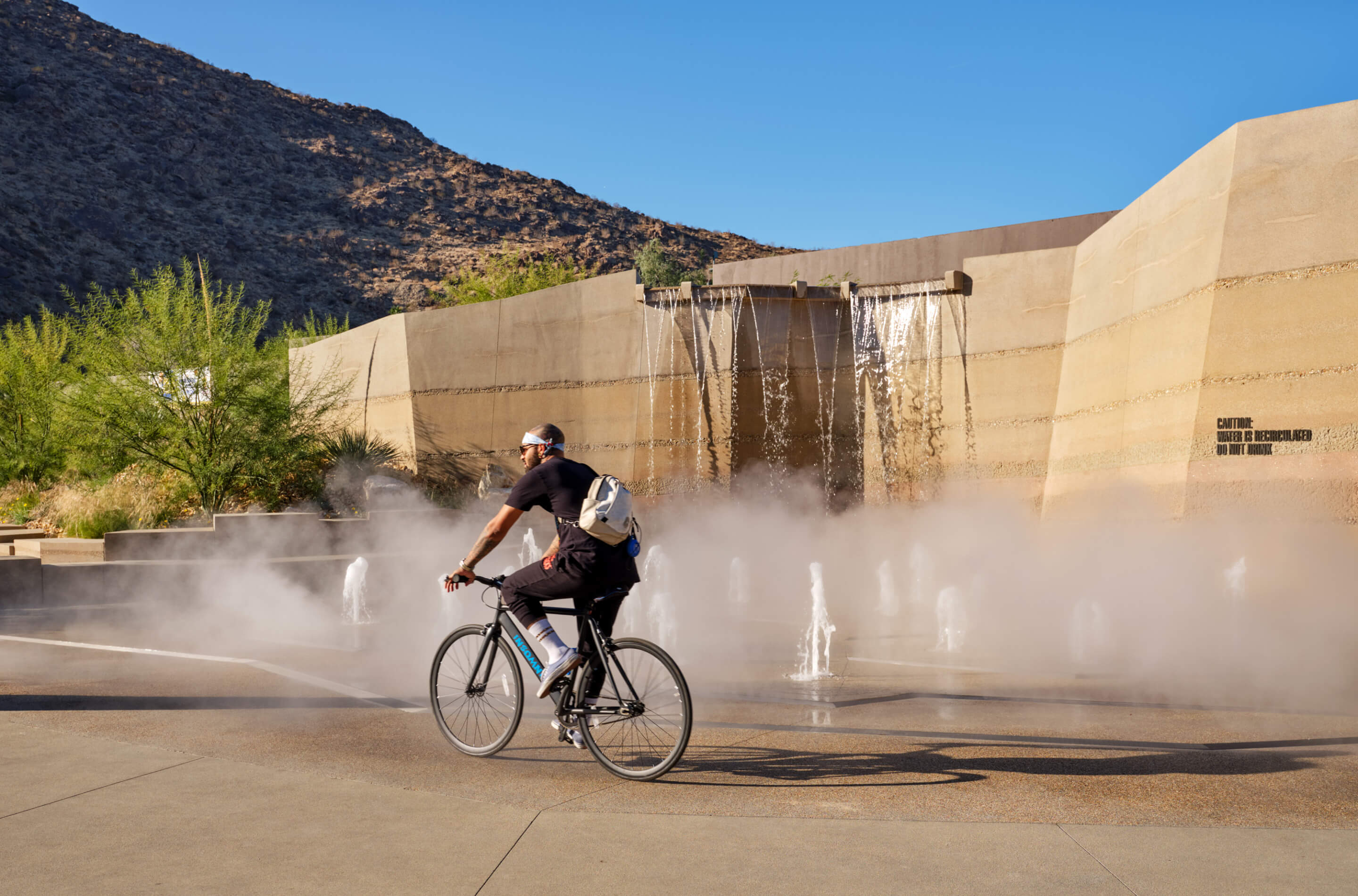 a man rides his bike past a misty water feature
