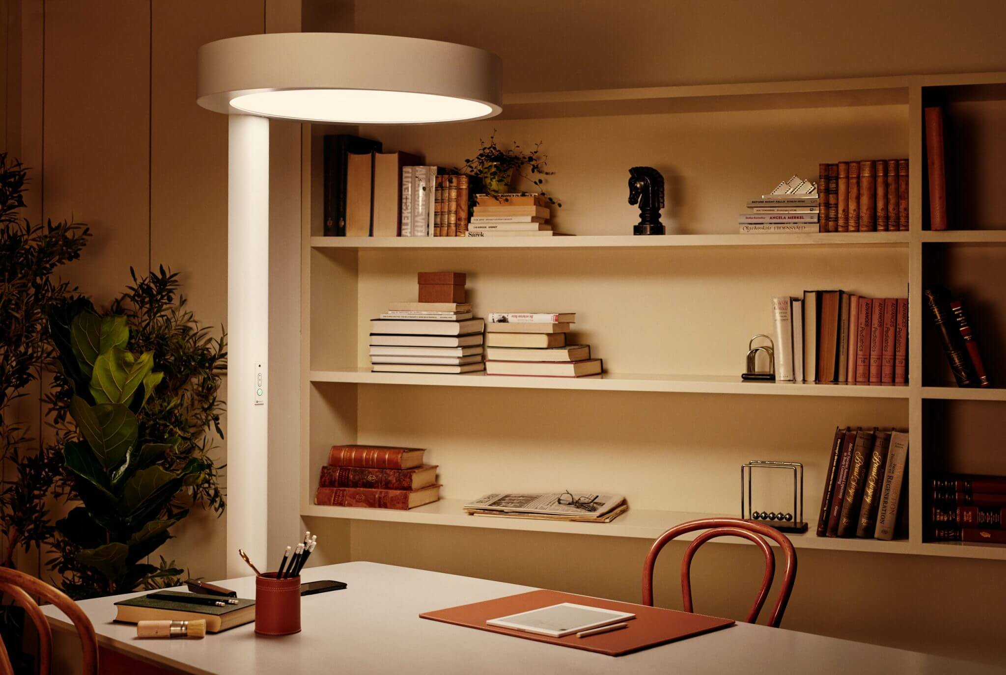 A white, circular standing lamp over a desk with a bookshelf in the background